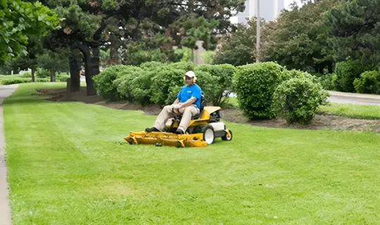 A man riding on the back of a yellow lawn mower.